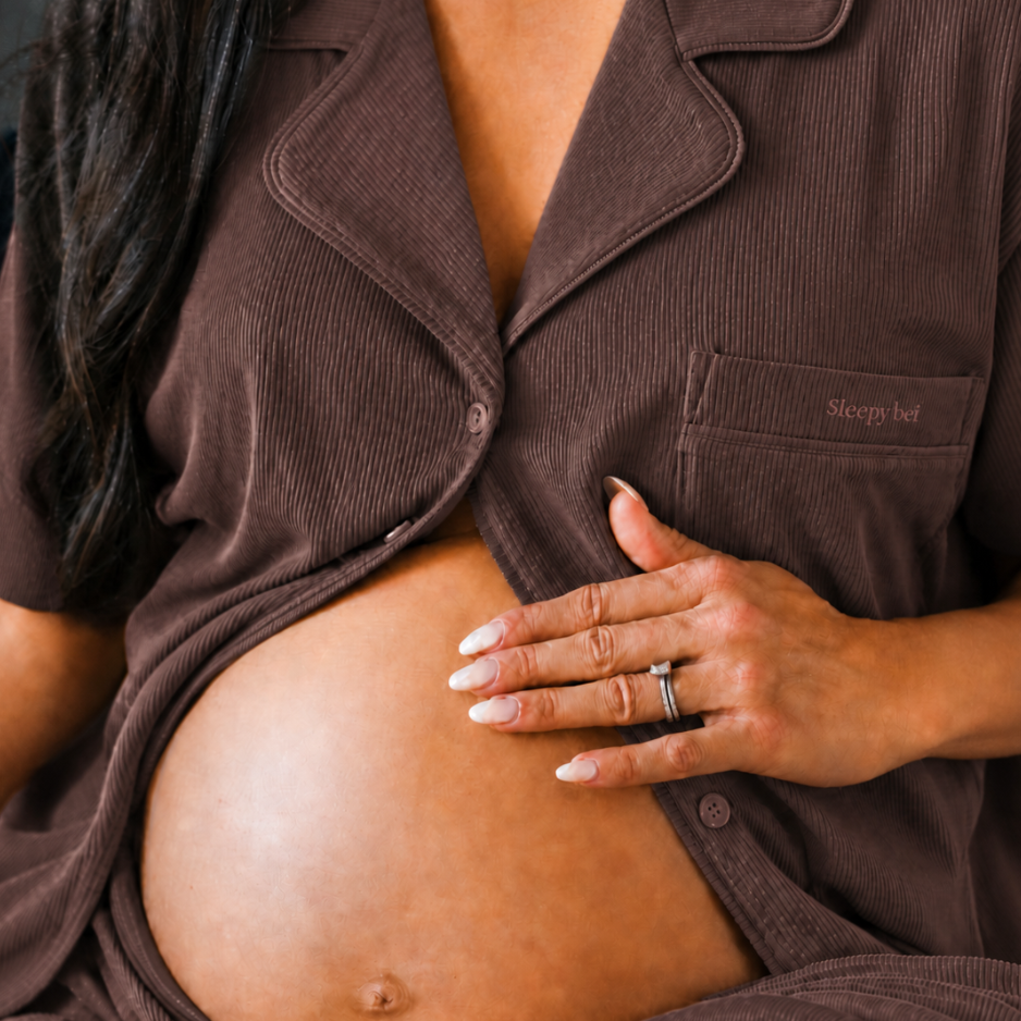 Close-up of the chocolate maternity pyjama top unbuttoned over a bare bump, hand resting gently on the belly
