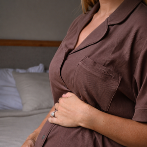 Side view of a mum-to-be in the chocolate maternity pyjama top, hand cradling her growing bump